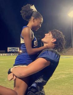 two girls are hugging each other on the football field at night with lights in the background