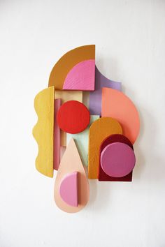 a clock made out of different shapes on a white wall with pink, orange and yellow accents