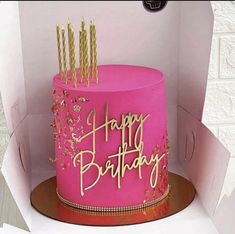 a pink birthday cake with gold candles in a box