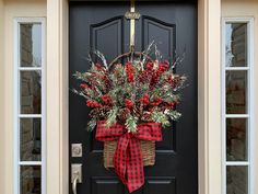 a black front door with a red and white christmas wreath hanging on it's side