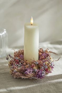 a white candle sitting on top of a table next to a vase with dried flowers