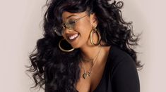 a woman with long black hair and gold hoop earrings smiling at the camera while wearing sunglasses