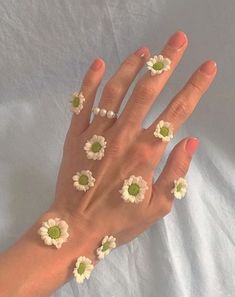 a woman's hand with white and green flowers on her fingers, all around them