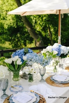 a table set with blue and white flowers in vases, plates and napkins