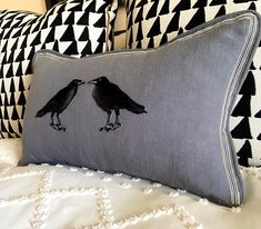 two black birds are touching each other on a gray and white pillow cover that is sitting on a bed