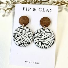 a pair of wooden earrings with black and white leaves on it, sitting next to a card