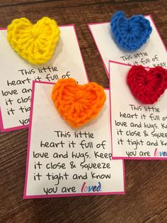 four crocheted hearts are displayed on cards with words written in the middle and below them