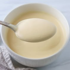 a spoon full of liquid sitting in a white bowl on top of a cloth covered table