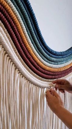 a woman is weaving a wall hanging made with yarns and cottons in different colors