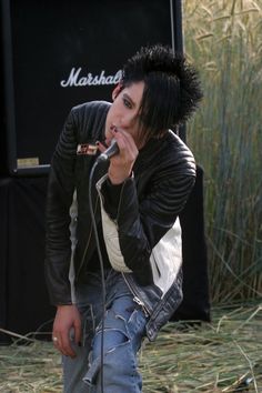 a man with black hair is singing into a microphone in front of a stage and grass