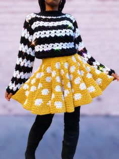 a woman wearing a yellow and black dress with white flowers on the skirt, standing in front of a brick wall