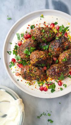 a white plate topped with meatballs covered in sauce and garnished with herbs