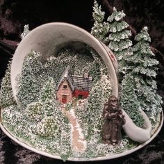 a miniature house in a bowl with trees and snow on the ground next to it