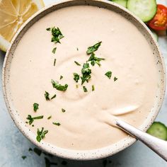 a white bowl filled with soup next to sliced cucumbers and lemon wedges