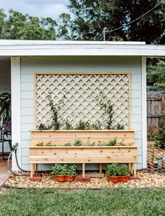 a wooden bench sitting in front of a white shed with potted plants on it