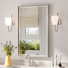 a white sink sitting under a bathroom mirror next to a vase with flowers on it