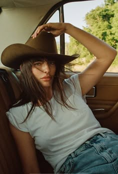 a woman sitting in the back seat of a car wearing a cowboy hat and jeans