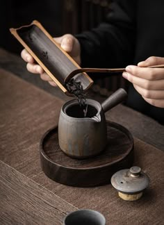 a person pouring tea into a cup on top of a wooden table