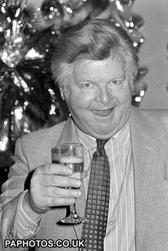 a man in a suit and tie holding a wine glass with a christmas tree behind him