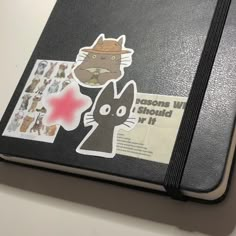 a black book with stickers on it sitting on a white counter top next to a laptop