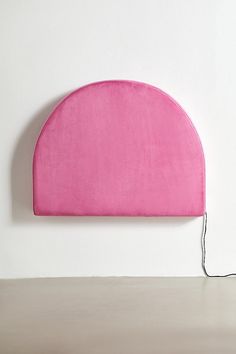 a pink headboard on a white wall next to a light bulb and plugged in