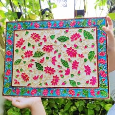 a person holding up a colorfully decorated tray in front of some plants and trees