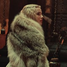 a woman in a fur coat is sitting on a swing and looking off into the distance