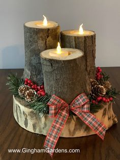 three candles are sitting on top of a tree stump with pine cones and red berries