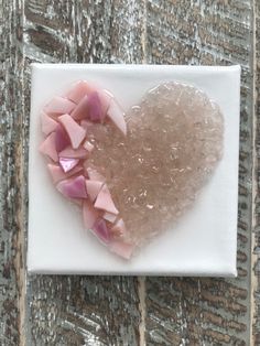 a heart shaped piece of glass sitting on top of a white square plate with pink petals