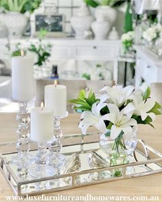 white flowers and candles sit on a mirrored tray in front of a dining room table