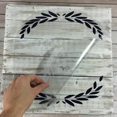 a hand is holding a piece of clear plastic over a wooden board with black leaves on it