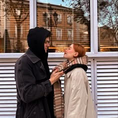 two people standing next to each other in front of a window with shutters on it