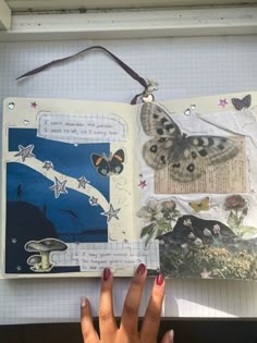 a person's hand is holding up an open book with butterflies on the pages