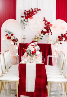 a red and white wedding set up with flowers on the head table, gold chairs