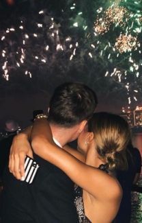 two people embracing each other while fireworks go off in the sky over water and buildings