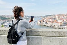 a woman standing on top of a cement wall holding a cell phone in her hand