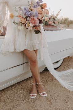 a woman standing next to a white car holding a bouquet