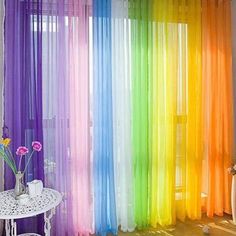 a rainbow colored curtain is hanging in front of a white table with flowers on it