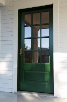 a green door on the side of a white house with glass panes in it