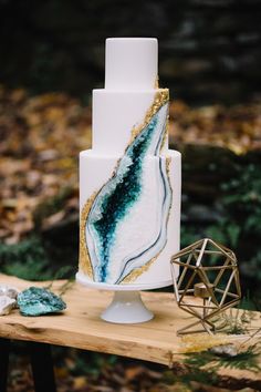 a white and gold wedding cake sitting on top of a wooden table in the woods