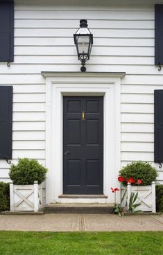 the front door of a white house with black shutters and two planters on either side