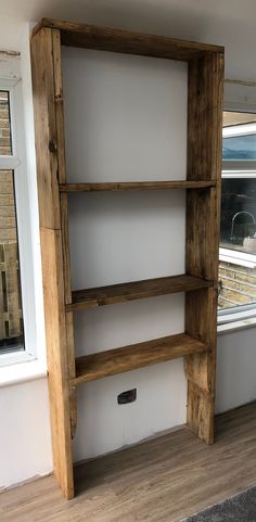 a wooden bookcase sitting in front of a window next to a white painted wall