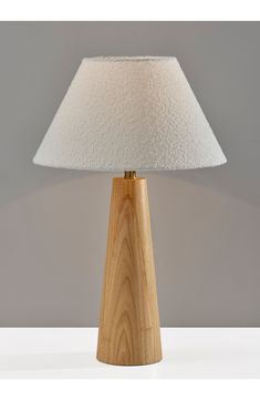 a wooden table lamp with a white fabric shade on the top and bottom, against a gray background