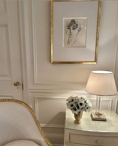 a white chair sitting next to a table with a lamp on top of it and a painting above it