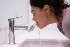 a woman is drinking water from a faucet