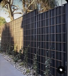 a black fence with rocks and plants on the side next to it in front of a tree