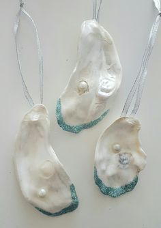 three white ceramic ornaments hanging from strings on a table with silver ribbon around the edges