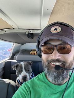 a man sitting in an airplane with a dog on his lap and wearing headphones