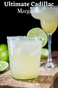 two margaritas sitting on top of a wooden cutting board with lime slices around them