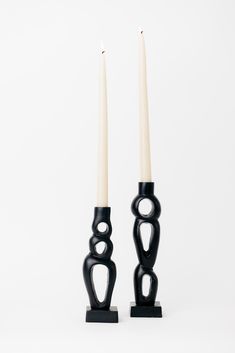 two black candlesticks sitting next to each other on top of a white surface